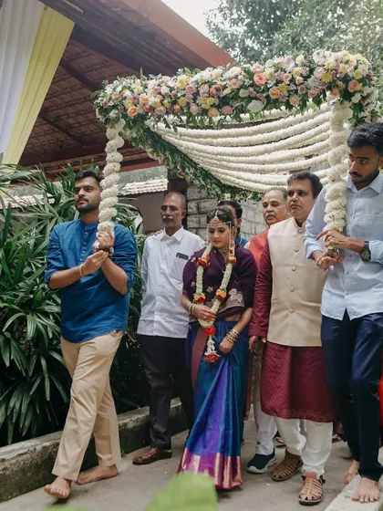 The bride's procession, walking with her family under a floral archway, a beautiful moment in a traditional South Indian wedding.