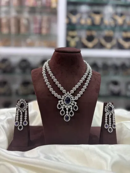 A double-layered AD necklace set with a central pendant. This versatile design comes in multiple colors including pink, white, emerald, and sapphire blue, making it a great addition to your inventory.