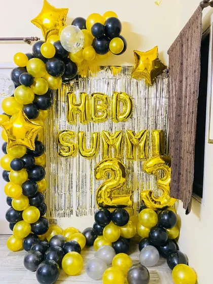 A 23rd birthday celebration with a black and gold balloon arch over a silver foil curtain.