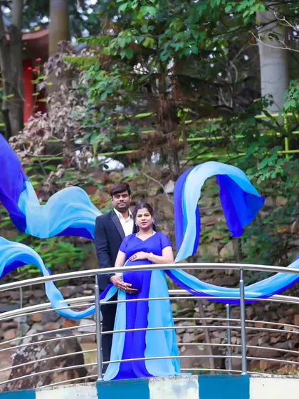 A stunning wide shot of a couple on a bridge, with the long, flowing trails of the blue maternity gown creating a dramatic effect.