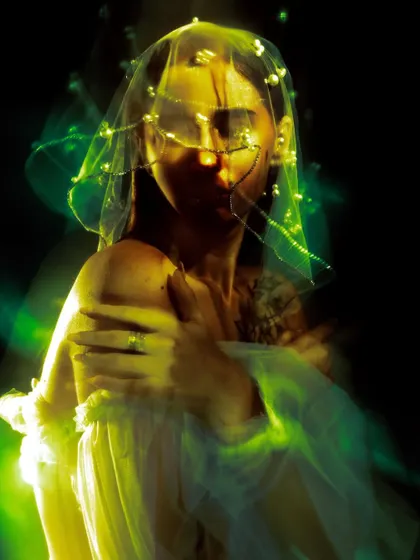 An experimental portrait using motion blur and yellow and green light filters. The model's face is a mysterious blur behind the illuminated veil, creating a ghostly and abstract image.