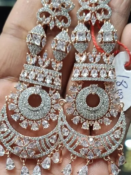 A pair of heavy chandbali earrings in rose gold polish, fully studded with American diamonds. The craftsmanship is very detailed, making them look like real diamond jewellery.