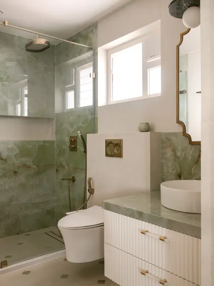 This bathroom for a client's daughter features soothing green onyx on the walls and countertop. We designed a custom floating vanity with a reeded front and acrylic and brass handles for a look that is fresh and modern.