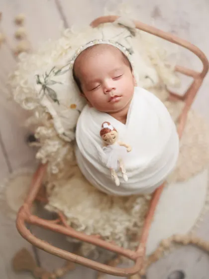 One month of pure wonder. This little one is peacefully asleep on a miniature sleigh prop, holding a tiny ballerina doll, creating a whimsical and sweet memory.