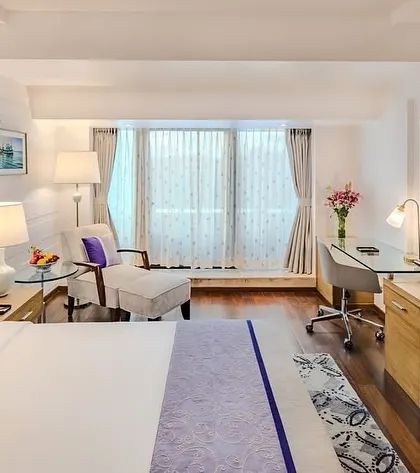 The bedroom area of the Taj Vivanta Goa suite, featuring a clean, modern aesthetic with pops of purple. The design includes a dedicated workspace and a comfortable lounge chair, catering to both leisure and business travelers.