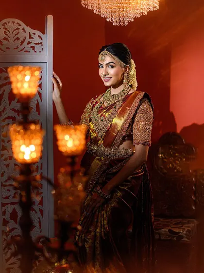 A portrait framed by glowing candle holders, creating an intimate and romantic mood. The bride's elegant pose and the rich colors of her attire are the centerpiece of the shot.