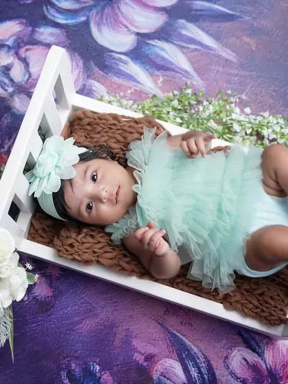 This two-month-old is looking angelic in a mint green outfit, resting in a miniature white crib against a dreamy floral backdrop.