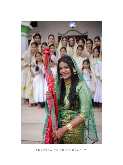 The bride holds a decorative staff as part of the Arikuth tradition, her smile radiating happiness.