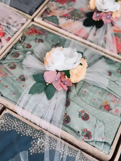 A close-up of a packed trousseau gift, showing a beautifully embroidered outfit wrapped in tulle and topped with a floral bouquet.