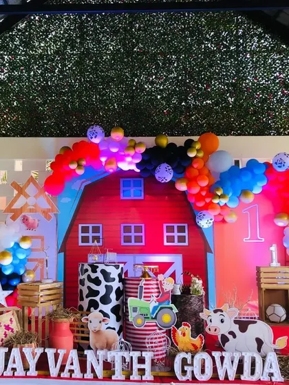 A fun and colorful farm theme for a first birthday. The centerpiece is a big red barn backdrop, surrounded by cute farm animal cutouts and props like hay and a tractor.
