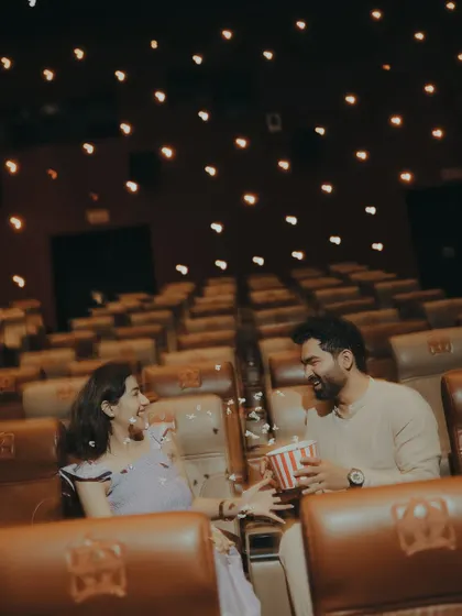 A playful moment sharing popcorn in a theatre. This shot adds a fun, candid element to the cinematic pre-wedding shoot, showing the couple's relaxed chemistry.