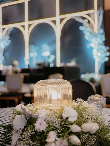 A close-up of a centerpiece from our modern black and white Sangeet. The fluted glass lamp surrounded by a wreath of baby's breath and white carnations added a soft, ambient glow to the tables.