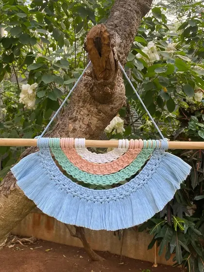 Our rainbow tapestry wall hanging adds a soft, whimsical touch to any room. This piece features pastel shades of blue, green, peach, and white, all handmade with macrame knots.