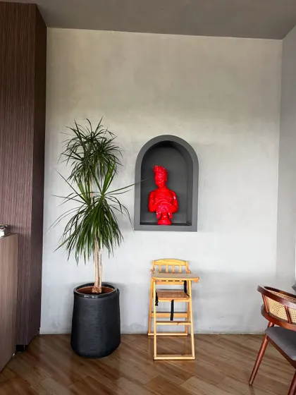 A Dracaena plant stands next to a modern art piece, showing how natural forms can complement artistic ones. The simplicity of the plant balances the boldness of the red sculpture.