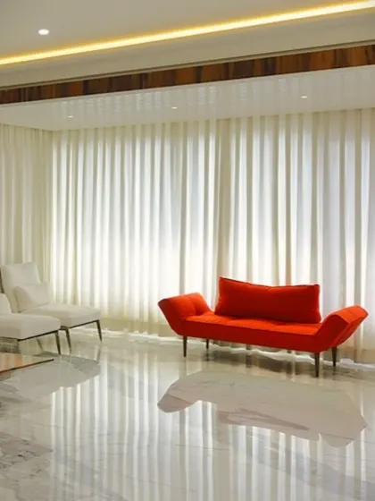 A bold red chaise lounge serves as a striking accent piece in this minimalist setting. The high-gloss marble floor reflects the sheer white curtains and accent furniture, creating a bright space where a single pop of color makes a powerful statement.