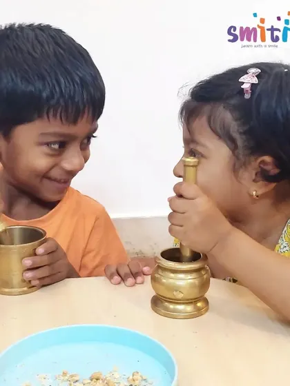A moment of shared joy and concentration as two children work with the mortar and pestle. Learning at Smiti is a social and collaborative experience.