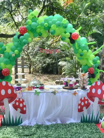 The main dessert table for a jungle-themed party, set under a large green balloon arch. The setup includes a custom cake, themed treats, and decorative elements like giant mushrooms.