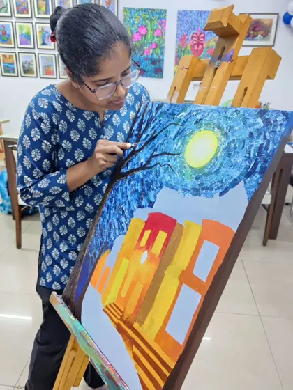 A student applies textured layers to her night scene painting. This image shows the hands-on process of building up a composition with a palette knife for a rich, tactile effect.