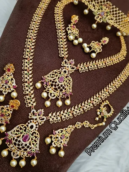A stunning AD and ruby combo set with an antique gold finish. This rental set includes two necklaces, earrings, and a maang tikka for a complete look.