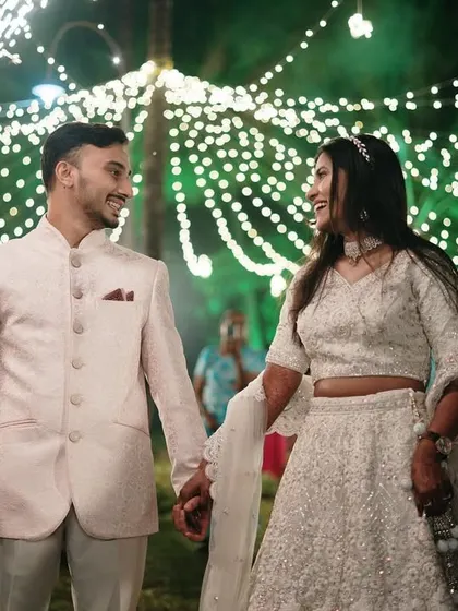 The couple's grand entrance under a canopy of fairy lights, holding hands and sharing a smile, with sparklers adding to the magical atmosphere.