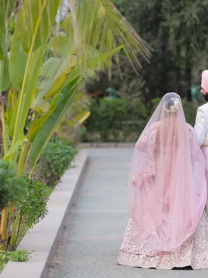 A classic shot of the bride and groom walking away from the camera, showcasing the beautiful details of their wedding attire against a lush green backdrop.