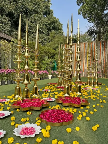 An artistic arrangement of brass spires and urlis filled with marigold and rose petals, creating a grand and traditional welcome aisle.