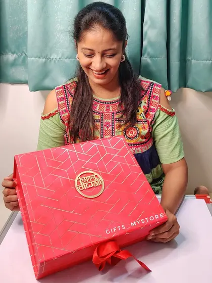 Here I am with one of our premium red Diwali hampers. The box itself is a keepsake, and it’s filled with festive items like a lotus diya, shubh labh hangings, and delicious treats.