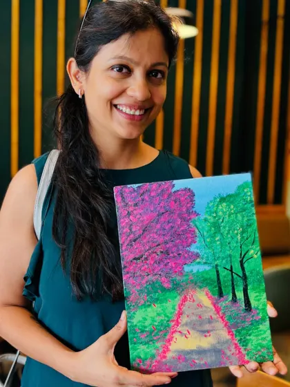 A participant beaming with pride as she holds up her beautiful spring blossom pathway painting.