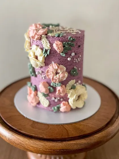 This tall barrel cake is a great example of my floral buttercream work. The textured purple frosting is adorned with hand-piped flowers in pastel pinks and yellows, creating a beautiful garden effect.