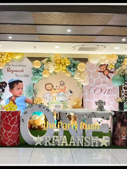 This wide shot of Riyaansh's "Wild One" party shows a complete jungle scene with large animal props and custom decor. The setup includes a large "ONE" marquee table, animal print plinths, and a full balloon arch, making it a truly immersive experience.