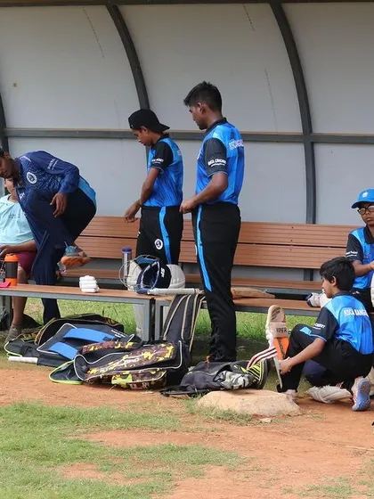 The dugout area during the Dasara Cup, with young players and their gear getting ready for the match.