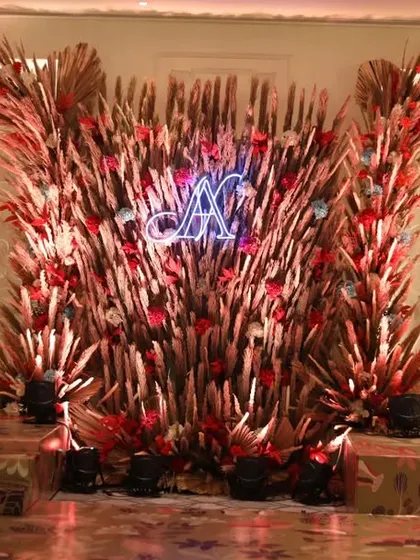 A stunning stage backdrop for a rustic-themed event, created with an explosion of dried pampas grass and leaves, with a custom neon sign.