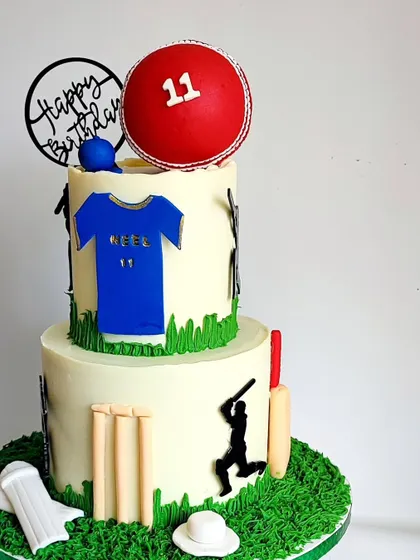 A side view of the cricket-themed cake, showing the player silhouettes and detailed fondant work against the smooth ganache.