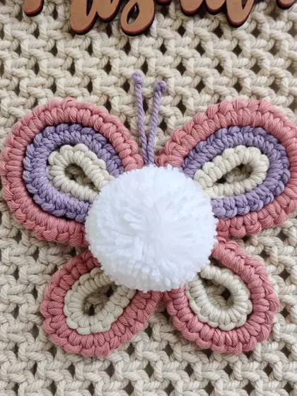 The butterfly detail, with its pink, purple, and cream wings and a fluffy pom-pom body.