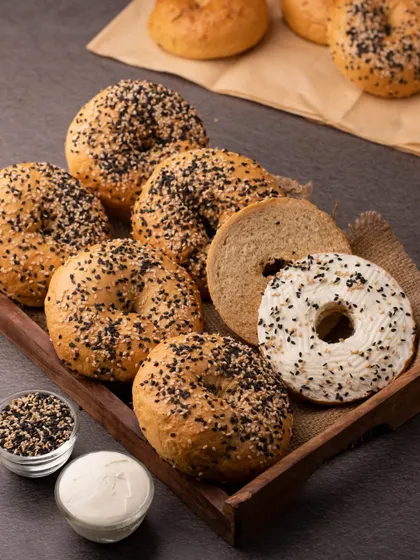 A tray of freshly baked bagels, some plain and some topped with cream cheese and sesame seeds. This shot showcases the product in a simple, appealing way, perfect for a bakery.