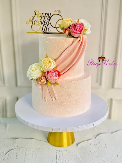 A sweet beginning to a beautiful forever. This two-tier anniversary cake in a soft pink hue features elegant draping and is adorned with fresh flowers for a classic, romantic look.