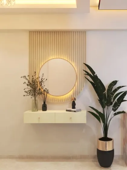 A chic and simple console setup in a foyer, with a round, backlit mirror, a floating drawer unit, and a large plant to add a touch of green.