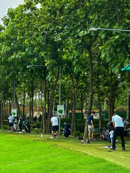 A wide shot of the driving range, bustling with activity and surrounded by lush greenery.