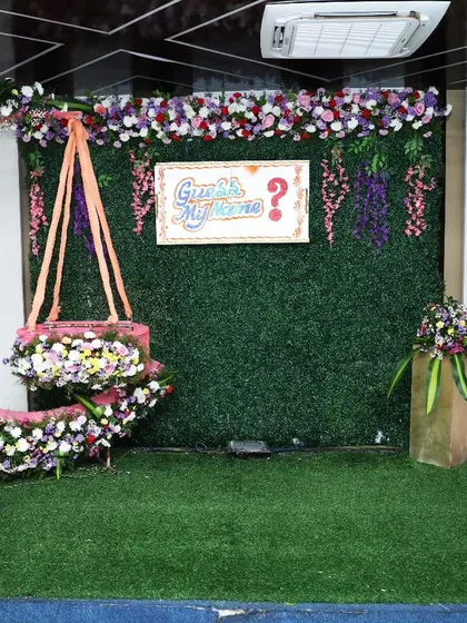 This floral decoration for a naming and cradle ceremony features a beautiful half-moon cradle adorned with flowers against a greenery wall. It's a perfect blend of modern and traditional styles.