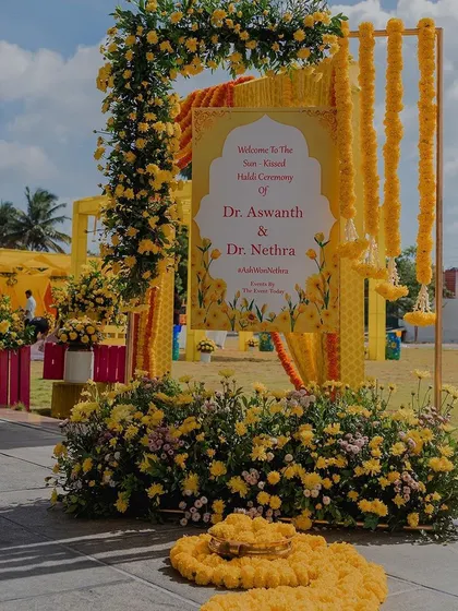 A grand entrance for a Haldi ceremony, featuring a welcome sign framed by a beautiful arch of yellow flowers.