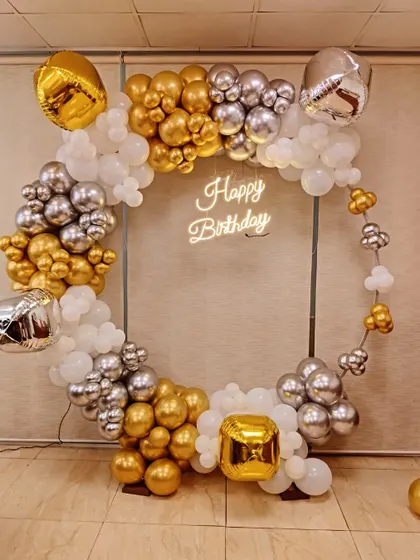 For a modern and chic birthday celebration, I design statement pieces like this circular frame with a custom 'Happy Birthday' neon sign. The organic balloon garland in gold, silver, and white adds a touch of elegance and is perfect for photos.