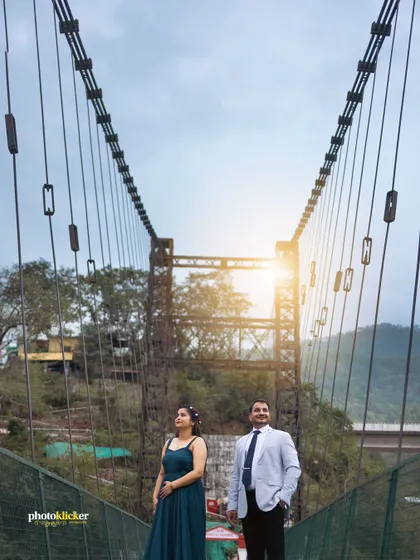 A powerful shot of a couple standing on a suspension bridge, framed by the bridge's cables, with the sun flaring behind them.