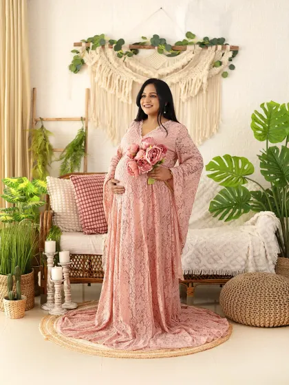 A radiant mom-to-be in a pink lace gown, holding a bouquet of matching flowers. This portrait in our boho setup is full of warmth and joy.