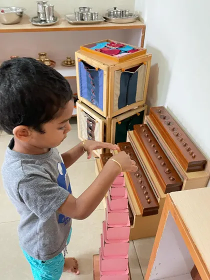 A child works with the Pink Tower, a classic sensorial material. This activity helps them visually discriminate between sizes and builds their understanding of dimensions, which is an indirect preparation for mathematics.