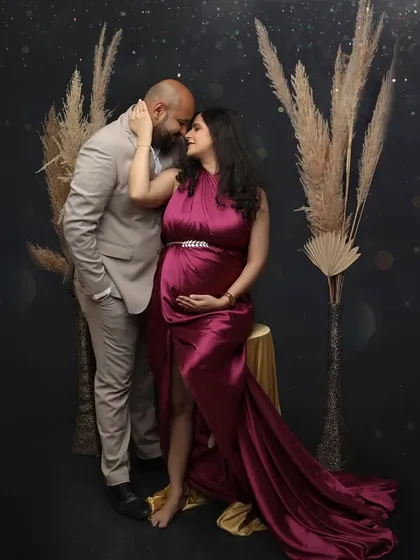 An intimate and romantic fine art portrait. This couple is posed closely against a dark background with pampas grass accents, the rich magenta of her gown adding a pop of vibrant color.