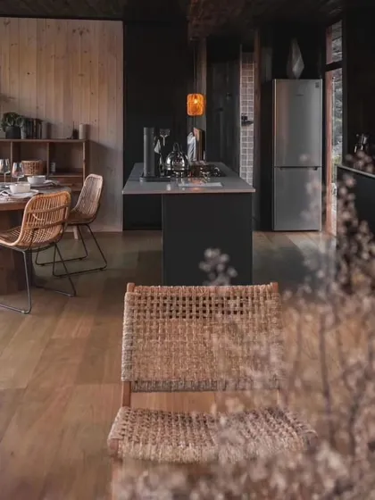 The dark, moody interior of this cabin creates a cozy and intimate atmosphere. The open-plan kitchen and dining area are perfect for socializing.