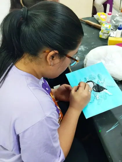 A participant outlining her clay bird design before painting. This workshop combines drawing, sculpting, and painting skills.