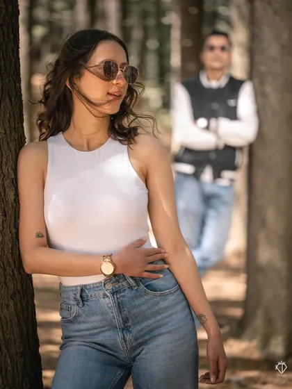 A stylish portrait with the woman in the foreground, leaning against a tree, and her partner blurred in the background, creating a sense of depth and story.