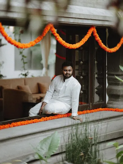 A beautifully composed shot of the groom seated on a windowsill, framed by traditional Indian decor.