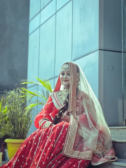 A full-length shot of a student's final bridal project. The model is posed on steps to showcase the flow and design of the red and gold lehenga, complete with a sheer veil.